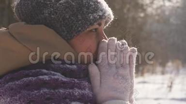 一位在户外散步的年轻女子在冬天的公园里散步时，她用手臂呼吸以<strong>保暖</strong>